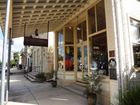 Two historic buildings in downtown Comfort — the 1913 Karger Building, formerly a pool hall (foreground), and the Ingenhuett-Karger Saloon building (stone building in background) — house The Elephant Story, a shop that sells Asian artisan goods
